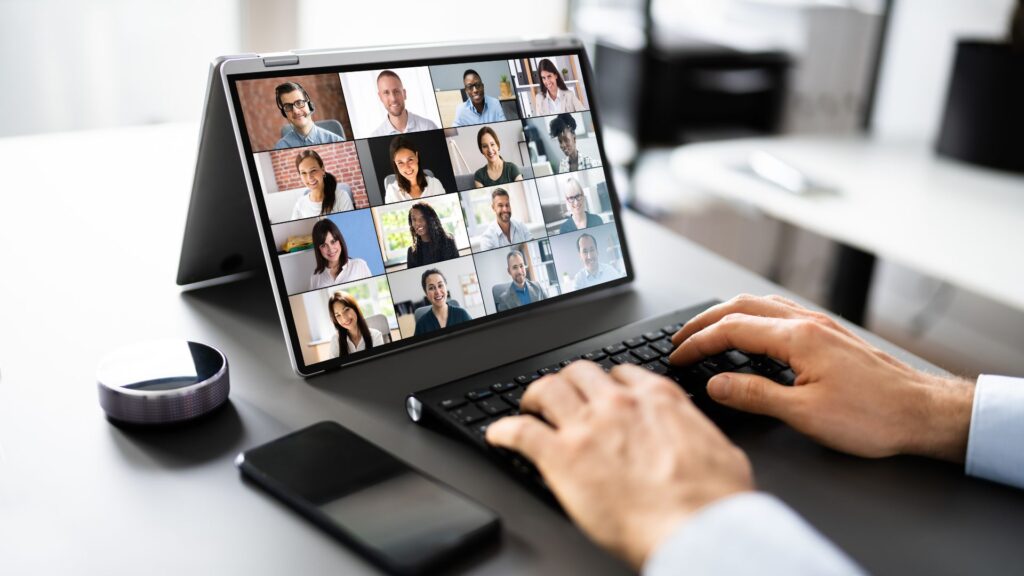 Führen im mobilen und hybriden Arbeiten: Führungskraft vor einem Bildschirm mit digitalen Teilnehmern eines Meetings